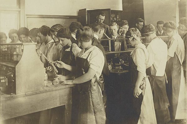 Sepia photograph of students wearing aprons and working at lab benches