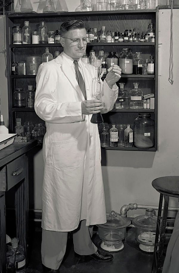 A chemistry professor holds glassware while he stands in his lab
