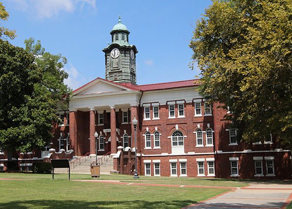 A red brick academic building with columns and a green clock tower