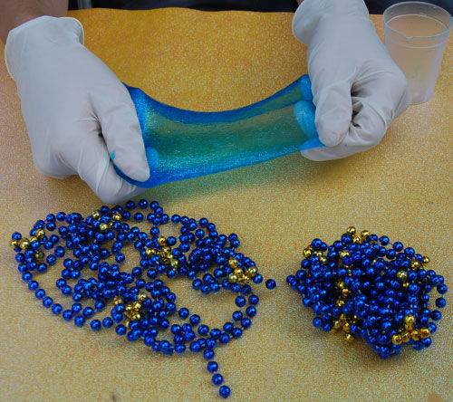 A pair of gloved hands stretching out blue slime, mardi gras beads in the foreground
