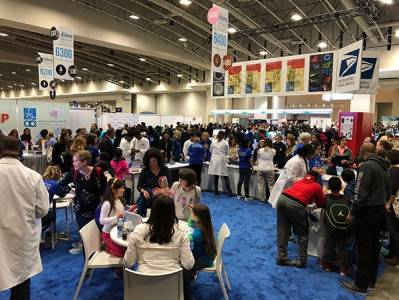 Families visiting walk-by tables at the USA Science & Engineering Festival in a large expo hall