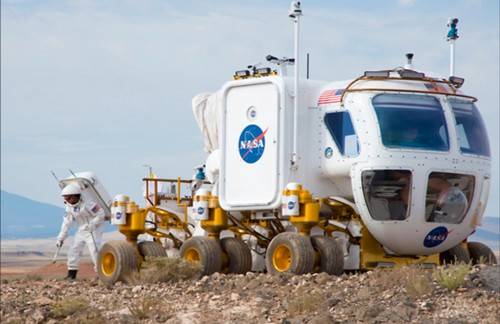NASA scientist wearing a space suit and performing field tests next to a space exploration vehicle in the Arizona desert.