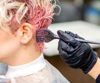 gloved hand applying pink hair dye