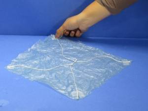 Taping four strings to plastic bag square to make parachute.