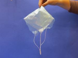 Holding plastic bag parachute with strings and paper clip attached
