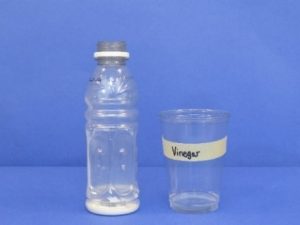 Baking soda in bottle and vinegar and detergent in cup.