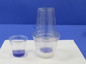 Cup with blue indicator placed in cup with vinegar and baking soda reaction with an upside down cup on top.