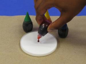 Adding one drop of food coloring to shallow container of glue.