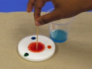 Touching toothpick with detergent on it to center of food coloring.