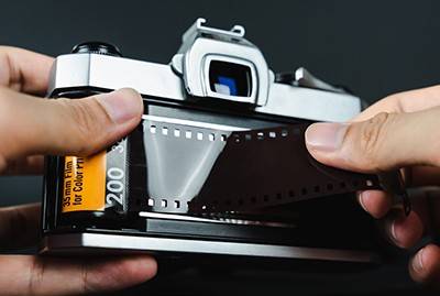 A photographer loads a roll of 35mm film into the back of a camera