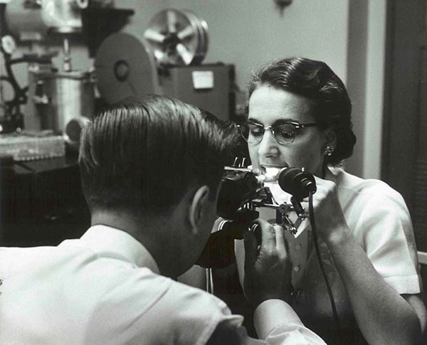A technician looks at a volunteers teeth through a microscope and using ultraviolet light