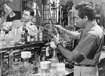 Black and white photograph of Stahmann and Link working in a biochemistry laboratory, surrounded by glassware