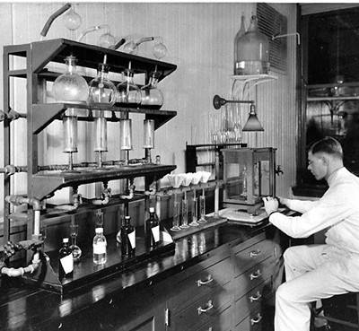 A chemist sits at a lab bench, surrounded by glassware and other apparatuses