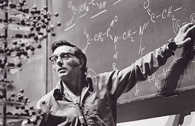George Pimentel in front of a chalkboard with chemical structures written in chalk