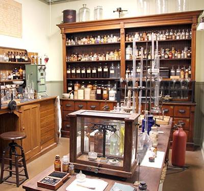 1900s laboratory reproduction: wooden cabinets with glass bottles of chemicals and other glassware throughout