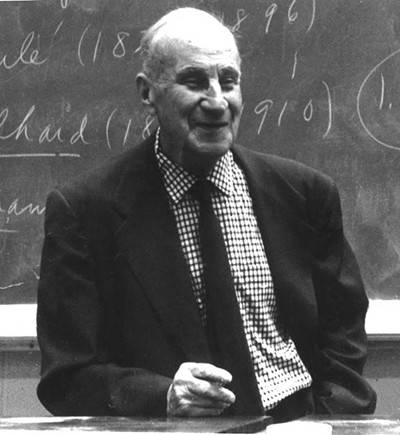 Black and white photo of Ralph Oesper, a man wearing a suit and tie, in front of a blackboard with chalk writing on it