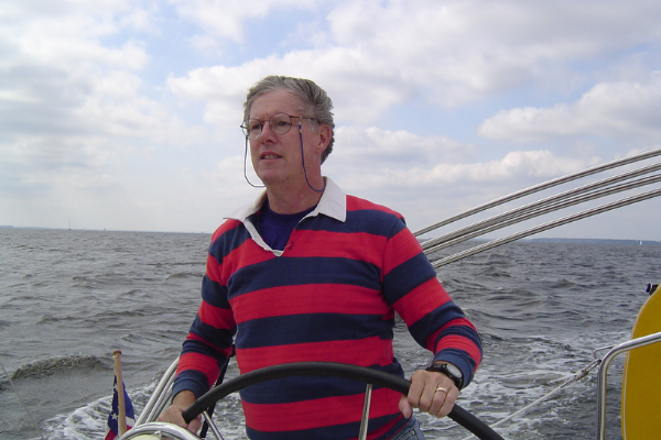 Eric C. Bigham, wearing a red striped shirt, steering the helm of a small ship.