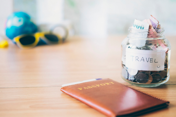 Passport on a table next to jar with money labeled "travel"