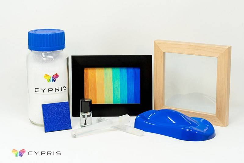 Figure 1. 1kg Jar of Cypris’ white powder (top left), Cypris’ rainbow colors (center black frame), framed glass window which blocks >30% of solar radiation (top right), samples (bottom) including painted roughened plastic, 3D objects, paint markers, and nail polish.