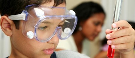 Boy in goggles looking at a glass vial of red liquid