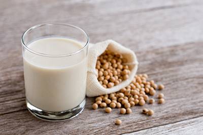 A short glass of soy milk next to a bag of soy beans