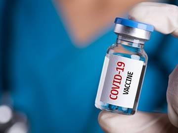 Gloved hand holding vial labeled "COVID-19 vaccine"