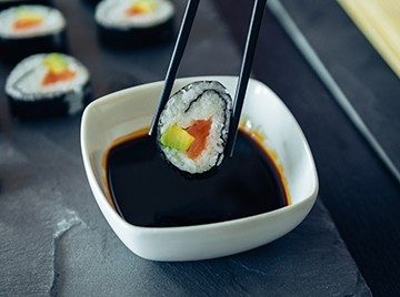 Chopsticks holding a sushi roll above a bowl of soy sauce