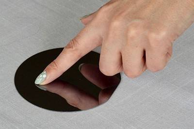 A person's hand touching a round, shiny disc with their pointer finger