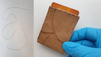 On the left, several pieces of yarn made from fungal fibers; on the right, a gloved hand holding a wallet made from fungal leather