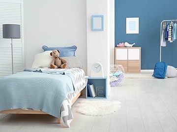 A children's bedroom, decorated in shades of blue with a teddy bear on the bed and a clothing rack in the background