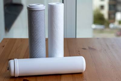 Two white filter cartridges stand upright behind a third white filter cartridge that’s laying down on a wooden counter.