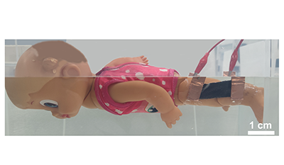 A doll facedown in the water with a black sensor attached to its knee.