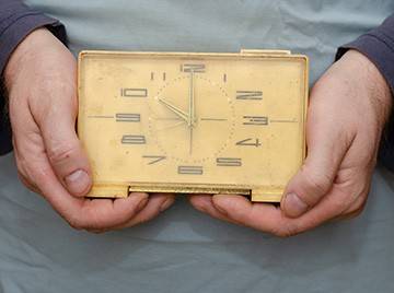 A person's hands holding an old clock made of yellowed plastic
