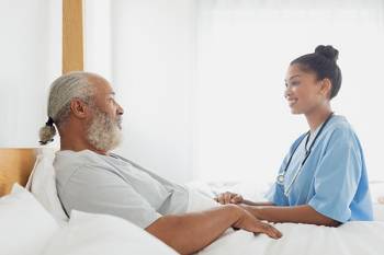 An older Black man sitting up in a hospital bed is looking at a physician.