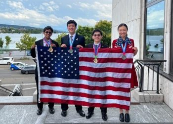 Four students showing off their Chemistry Olympiad medals and holding an American flag.