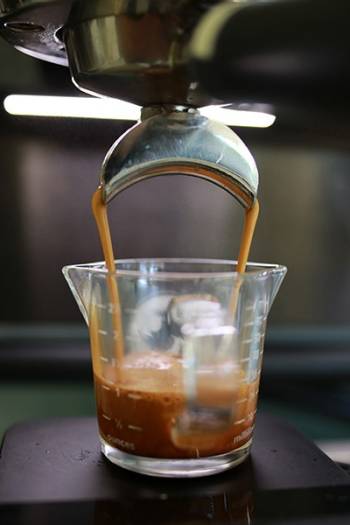 An espresso machine brews coffee into a glass measuring cup. 
