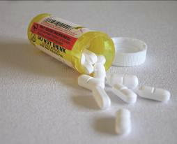 An open prescription medication bottle with white pills spilling out onto a surface.