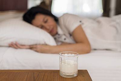 person sleeping with glass of milk on table next to bed