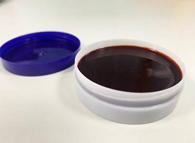 A shallow, white container holds a dark red cream