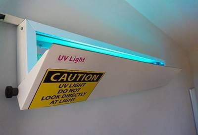 A white metal box labeled “UV light” is positioned at the top of a wall and shines blue ultraviolet light toward the ceiling.