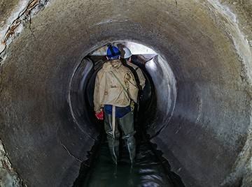 Two workers wearing helmets and waterproof boots walking away and down a sewer tunnel