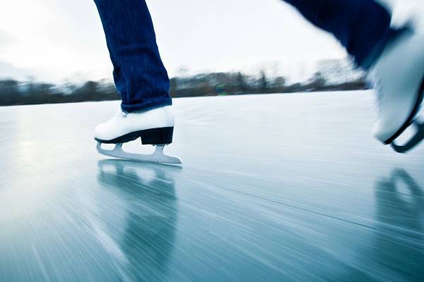 Close-up of ice skater's skates moving over a frozen sheet of ice