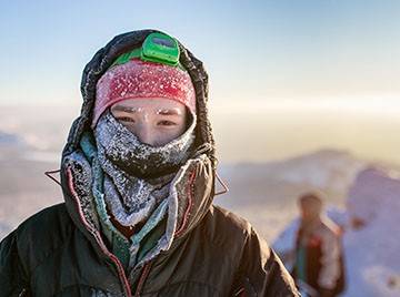 Alpinist wrapped up cold weather layers in a sunny but winter mountain vista