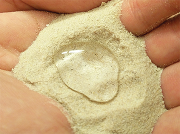 Person's hand holding a palm full of sand, with a large, intact water droplet on top