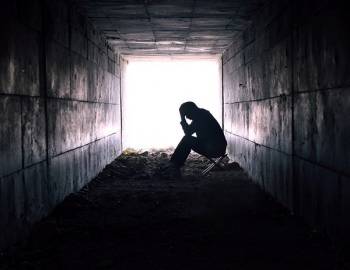 A person sits alone in a dark tunnel.