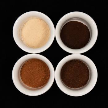 Four white cups holding different colored lab-grown coffee powders. The powders are light tan, a dark brown that’s almost black, dark brown and a reddish brown.