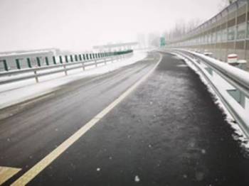 A snowy road has a clear path in the middle where black asphalt is showing