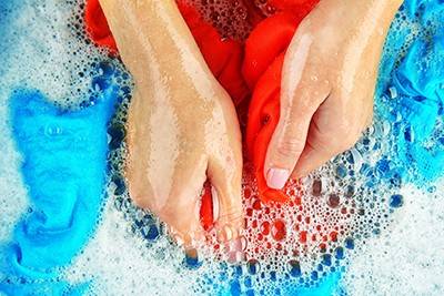 A person is washing a red article of clothing by hand in a tub of soapy water. 