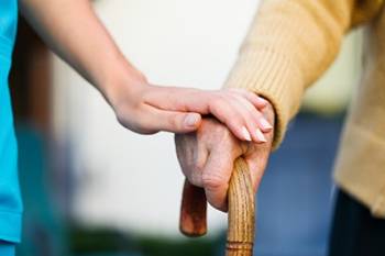 A doctor placing their hand atop an older person’s hand holding a cane.