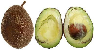 To the left sits a whole avocado with a dark brown, shiny peel. To the right, two halves of an avocado are shown with shiny green and slightly spotted brown pulp at the base.